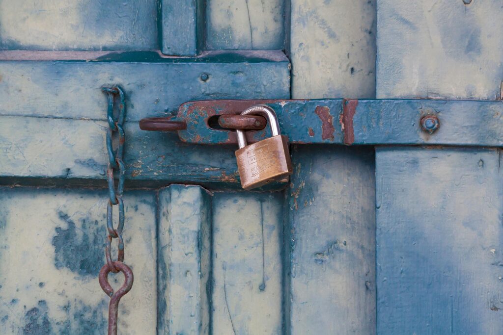 pexels-photo-164425-164425 A close-up of a rusty padlock securing a blue painted wooden door with chain and bolt.