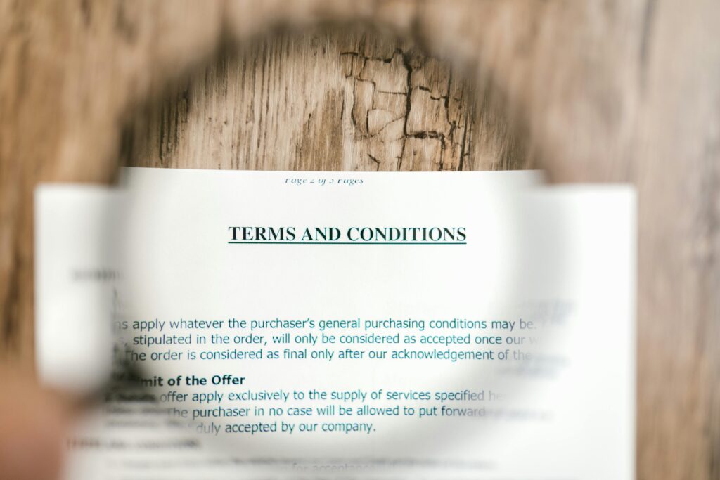 pexels-photo-7821937-7821937 Magnifying glass focusing on terms and conditions document on wooden surface.